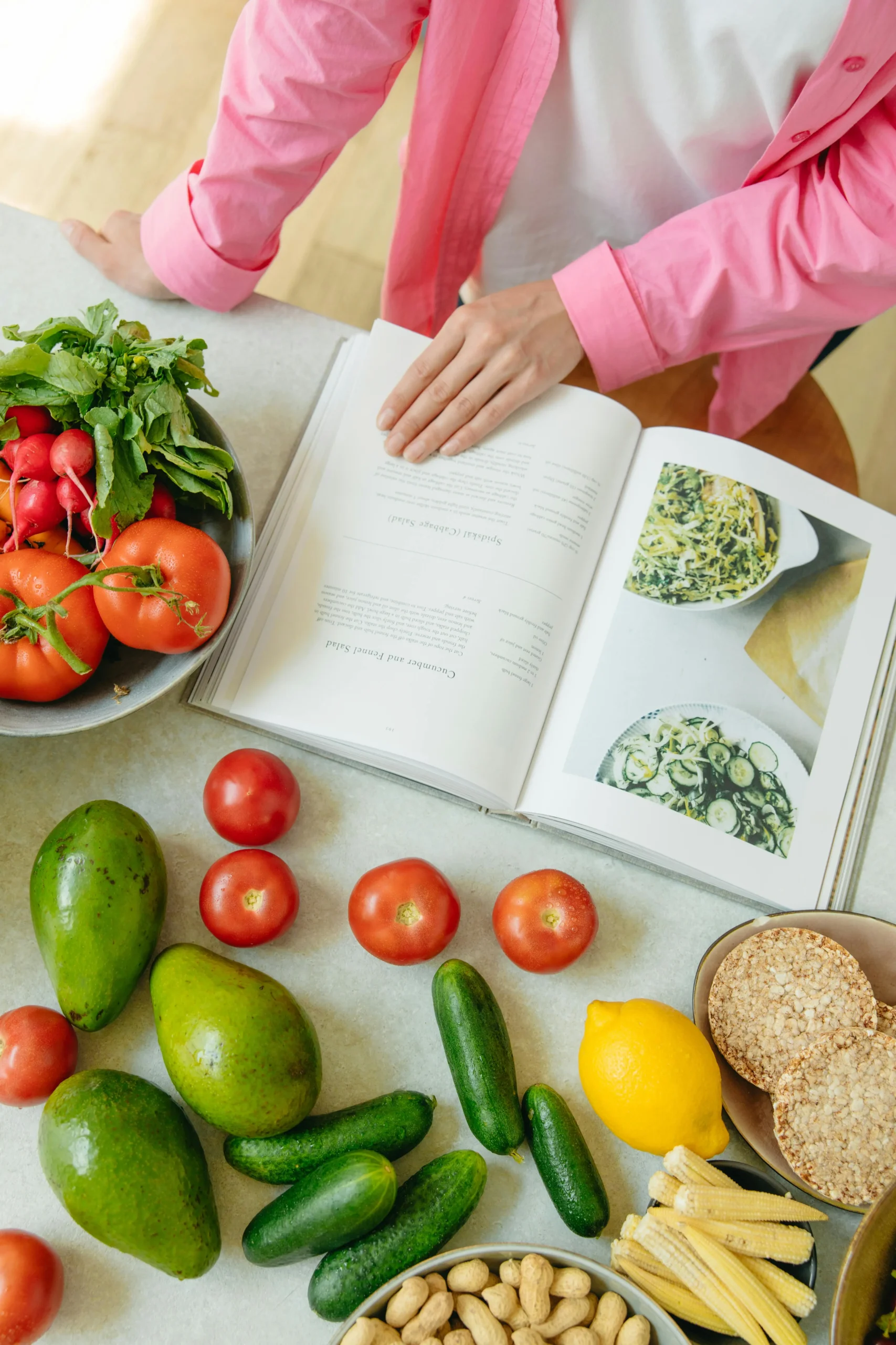 Livre de recettes ouvert à côté d'une variété de légumes frais, symbolisant une alimentation saine et la préparation de recettes.