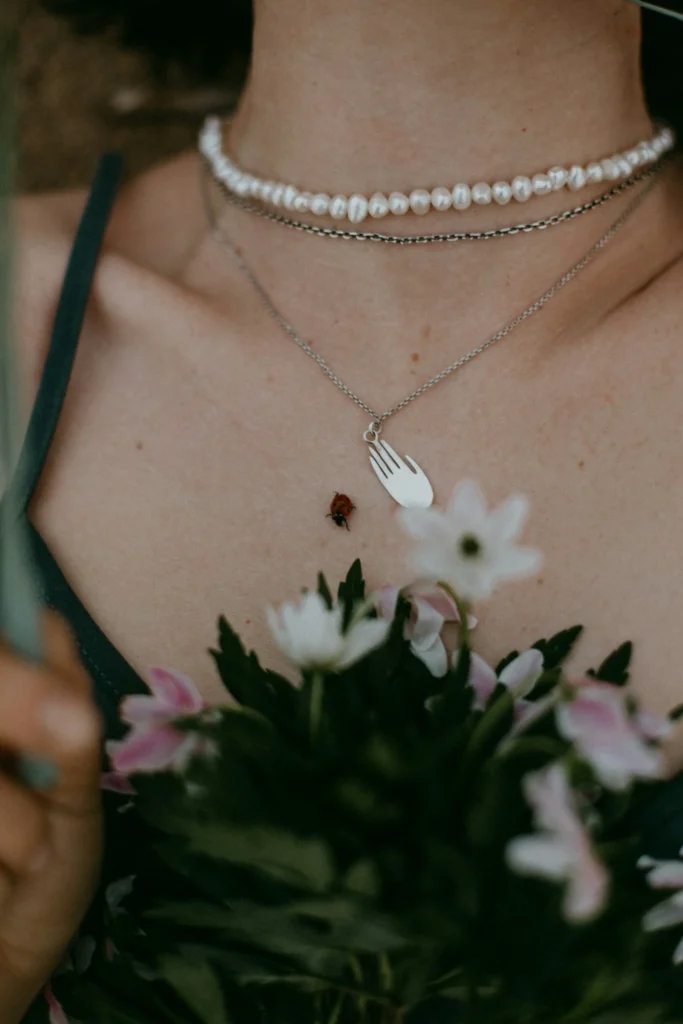 Détail d’un collier de perles avec un pendentif en forme de fourchette sur la poitrine d’une femme tenant des fleurs, représentant l’équilibre et la sérénité retrouvés par l’hypnothérapie à Jeumont